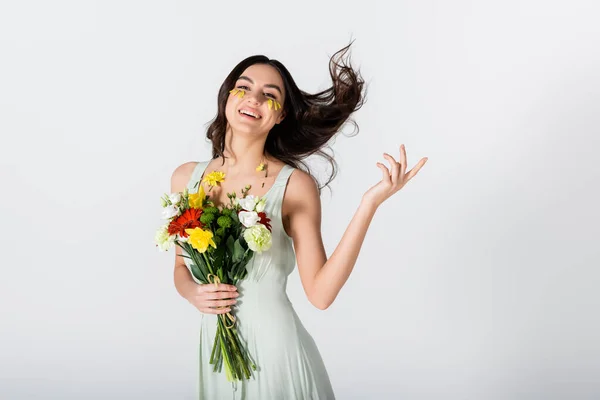 Cheerful young woman with petals on face holding bouquet of flowers isolated on white — Stock Photo