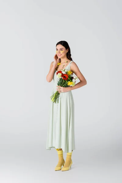 Full length of young woman with petals on face holding bouquet of spring flowers on white — Stock Photo