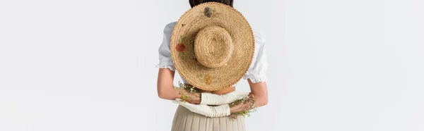 Partial view of woman in gloves with flowers and straw hat behind back isolated on white, banner — Stock Photo