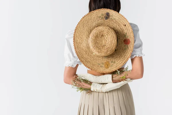 Vista parziale di giovane donna in guanti con fiori e cappello di paglia dietro la schiena isolato su bianco — Foto stock