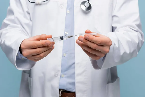 Cropped view of doctor in white coat holding syringe isolated on blue — Stock Photo