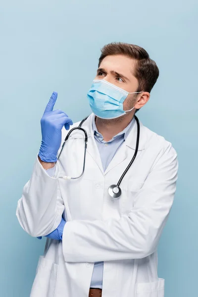 Médico en máscara médica y bata blanca con estetoscopio teniendo idea aislada en azul - foto de stock