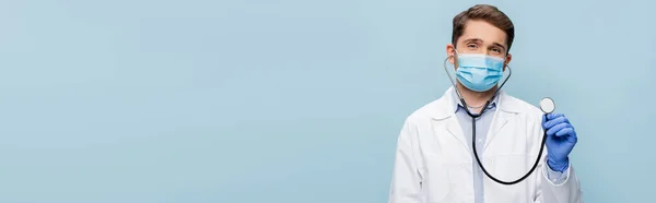 Médecin en masque médical et manteau blanc tenant stéthoscope isolé sur bleu, bannière — Photo de stock