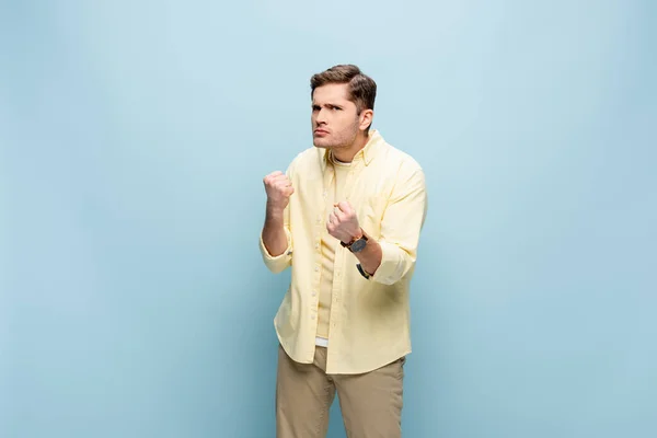 Angry young man with clenched fists looking at camera isolated on blue — Stock Photo
