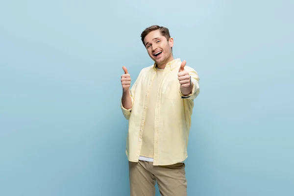 Positive young man in yellow shirt looking at camera and showing like isolated on blue — Stock Photo