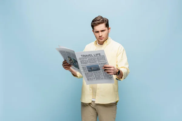 Joven serio en camisa leyendo periódico de viaje aislado en azul - foto de stock