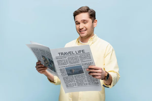 Pleased young man in shirt reading travel newspaper isolated on blue — Stock Photo