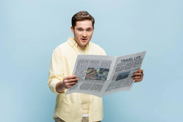 Surprised young man in shirt reading travel newspaper isolated on blue — Stock Photo