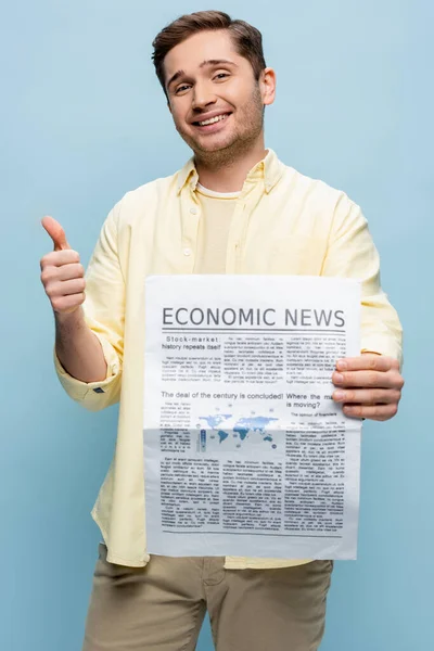 Happy young man in shirt holding economical newspaper and showing thumb up isolated on blue — Stock Photo