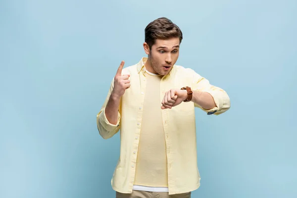 Jeune homme en chemise jaune regardant montre-bracelet et pointant vers le haut avec le doigt sur le bleu — Photo de stock