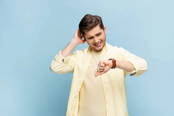 Inquiet jeune homme en chemise jaune regardant montre-bracelet sur bleu — Photo de stock