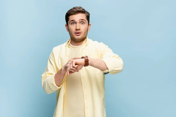 Homme inquiet en chemise jaune avec montre-bracelet à portée de main isolé sur bleu — Photo de stock