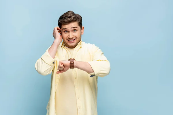 Stressed young man in yellow shirt with wristwatch on hand isolated on blue — Stock Photo