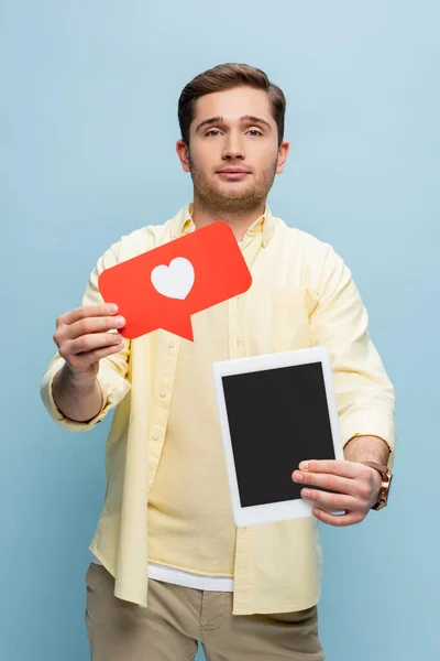 Homme en chemise tenant coeur en papier et tablette numérique avec écran blanc isolé sur bleu — Photo de stock