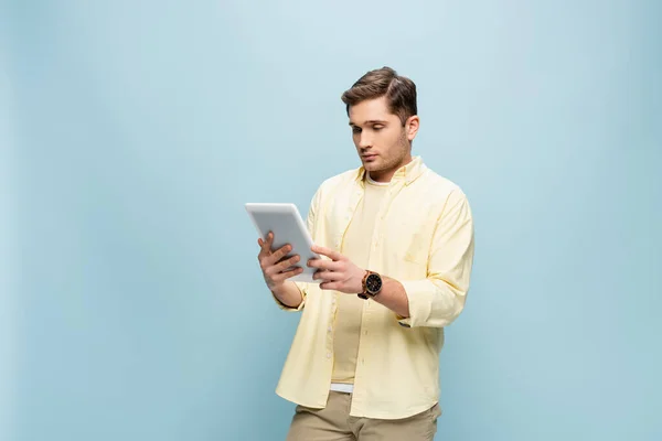 Young man in yellow shirt looking at digital tablet isolated on blue — Stock Photo