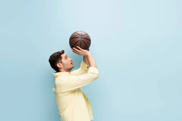 Вид сбоку человека в желтой рубашке, бросающего баскетбол на синий — стоковое фото