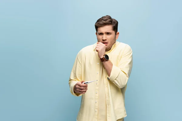 Sick man coughing and holding electronic thermometer on blue — Stock Photo