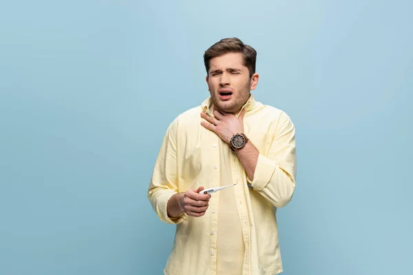 Sick man suffering from sore throat and holding electronic thermometer isolated on blue — Stock Photo