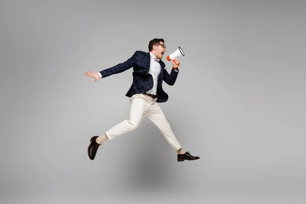 Full length of businessman jumping and screaming in megaphone on grey — Stock Photo