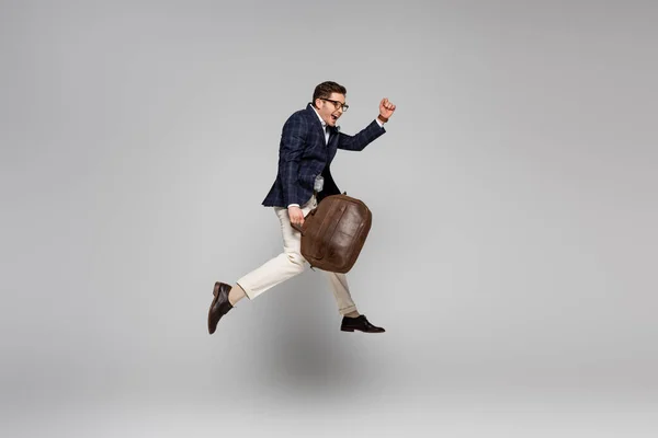 Full length of amazed businessman holding leather bag and levitating on grey — Stock Photo