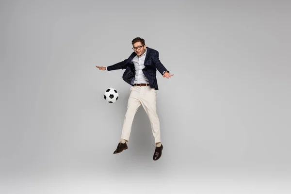 Piena lunghezza di uomo d'affari sorridente che gioca a calcio mentre levita sul grigio — Foto stock