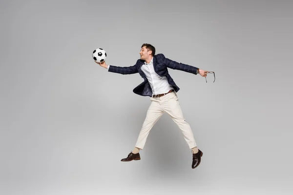 Volle Länge des lächelnden Geschäftsmannes, der eine Brille hält und Fußball spielt, während er auf grau schwebt — Stockfoto