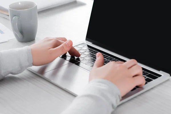 Vista ritagliata di freelance utilizzando laptop vicino tazza sul tavolo — Foto stock