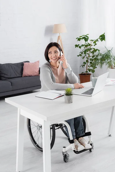 Behinderte Frau spricht auf Smartphone neben Laptop und Notebook auf Tisch — Stockfoto