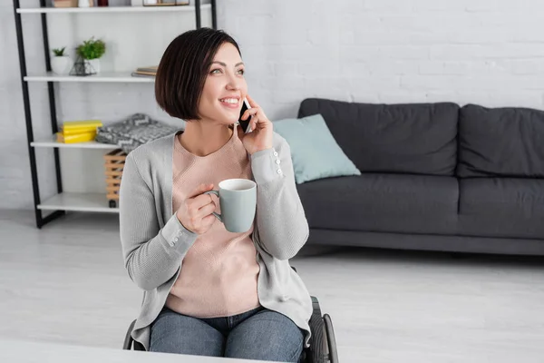 Behinderte Frau lächelt, während sie Tasse in der Hand hält und mit dem Handy spricht — Stockfoto