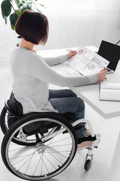 Vue latérale de la femme handicapée travaillant avec des graphiques sur des papiers près d'un ordinateur portable — Photo de stock