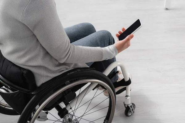 Cropped view of disabled woman in wheelchair holding smartphone with blank screen at home — Stock Photo