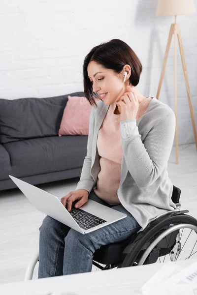 Lächelnde Frau im Rollstuhl mit Kopfhörer und Laptop im Wohnzimmer — Stockfoto