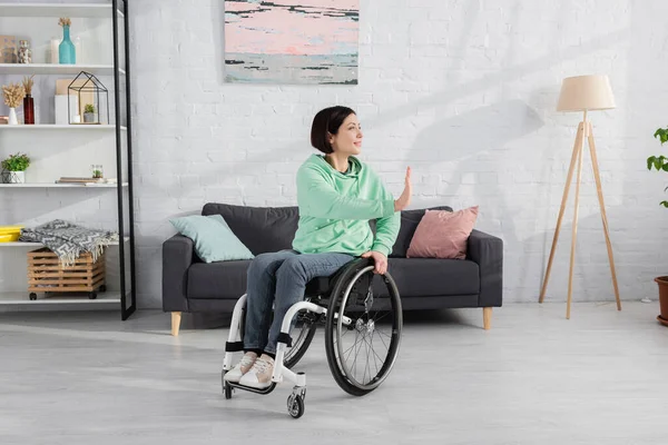 Smiling woman in wheelchair exercising near couch at home — Stock Photo