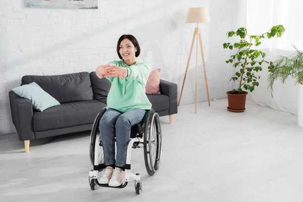 Positive woman in wheelchair stretching during training at home — Stock Photo
