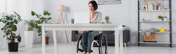 Freelancer in wheelchair using laptop near cup at home, banner — Stock Photo