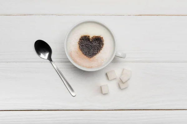 Top view of cup with cappuccino near spoon and sugar cubes on white wooden background — Stock Photo