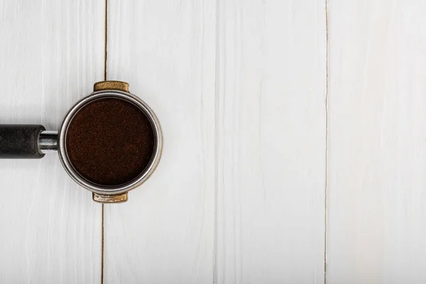 Top view of metallic portafilter with fresh ground coffee on white wooden surface — Stock Photo