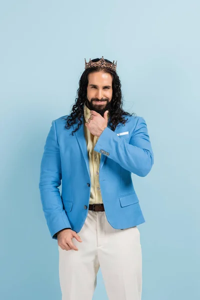 Homme hispanique barbu en couronne et veste souriant isolé sur bleu — Photo de stock
