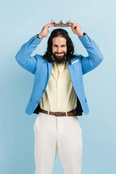 Bearded hispanic man in jacket wearing crown and smiling isolated on blue — Stock Photo