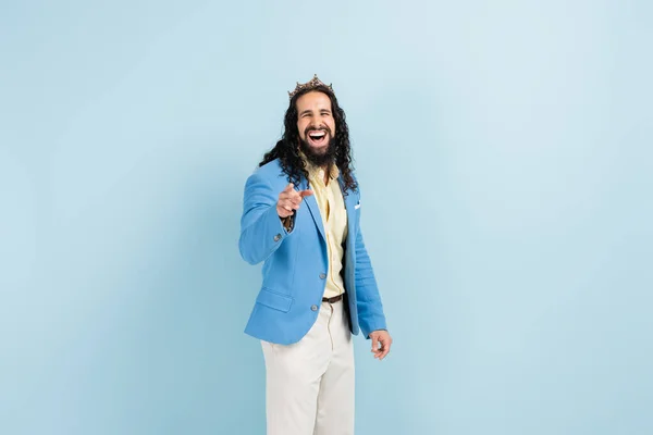 Bärtiger hispanischer Mann in Krone und Jacke lacht, während er mit dem Finger auf blau zeigt — Stockfoto