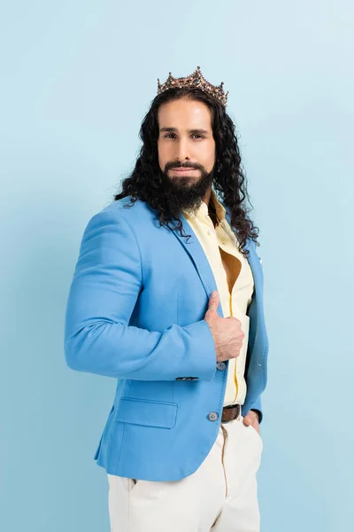 Bärtiger hispanischer Mann in Krone und Jacke posiert isoliert auf blauem Grund — Stockfoto