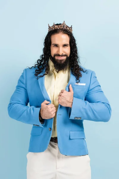 Веселий іспаномовний чоловік у коронці, що регулює куртку ізольовано на синьому — стокове фото