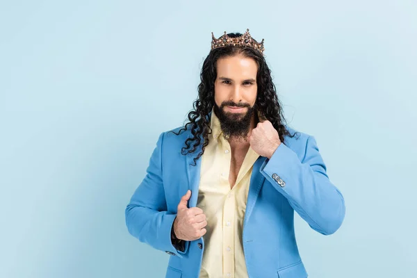Hombre hispano barbudo en la corona ajustando chaqueta aislado en azul — Stock Photo