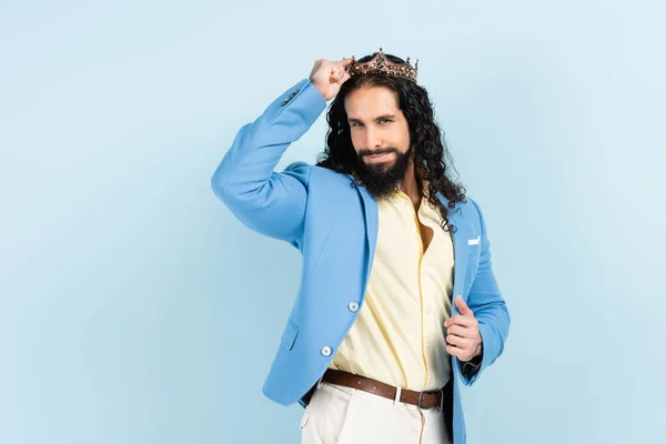 Hombre hispano barbudo y rizado en chaqueta ajustando corona aislado en azul — Stock Photo