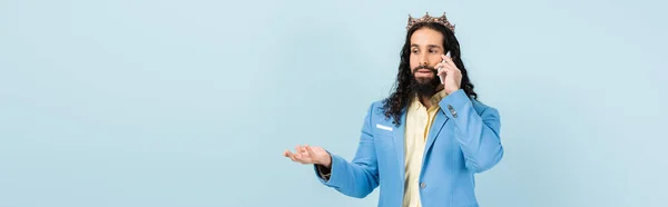 Hombre hispano barbudo con chaqueta y corona hablando en teléfono inteligente aislado en azul, pancarta — Stock Photo