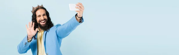 Homem hispânico feliz na jaqueta e coroa segurando smartphone e ter chamada de vídeo isolado em azul, banner — Fotografia de Stock