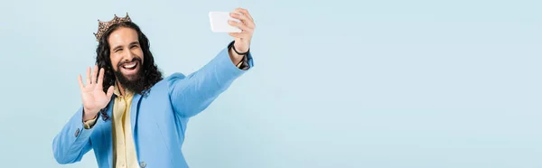 Felice uomo ispanico in giacca e corona che tiene smartphone e avere videochiamata isolata su blu, banner — Foto stock