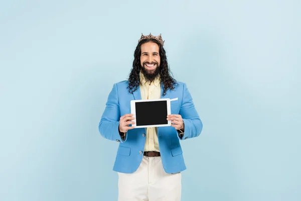 Щасливий іспаномовний чоловік в куртці і короні тримає цифровий планшет з порожнім екраном ізольовано на синьому — стокове фото