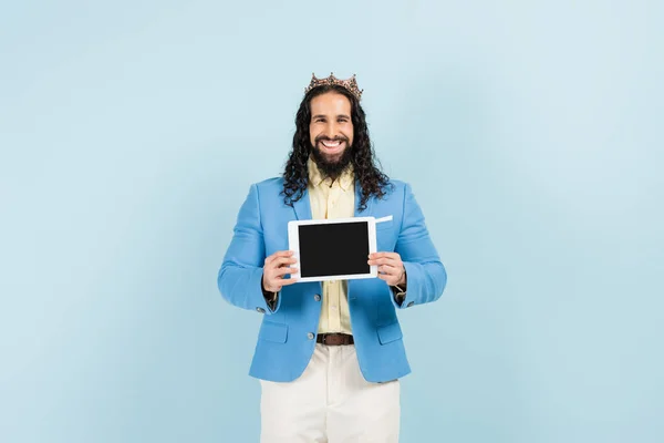 Hombre hispano feliz con chaqueta y corona sosteniendo tableta digital con pantalla en blanco aislado en azul — Stock Photo