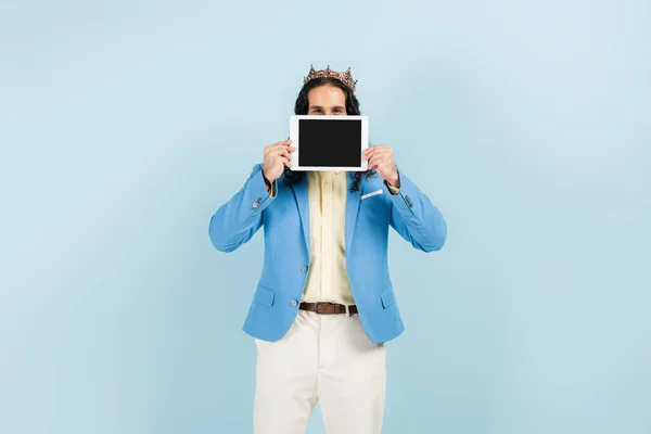 Hombre hispano con chaqueta y corona sosteniendo tableta digital con pantalla en blanco aislada en azul — Stock Photo